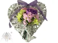 Bílé proutěné závěsné srdce zdobené fialovou růží, růžovými a zelenými květy a fialovou mašlí