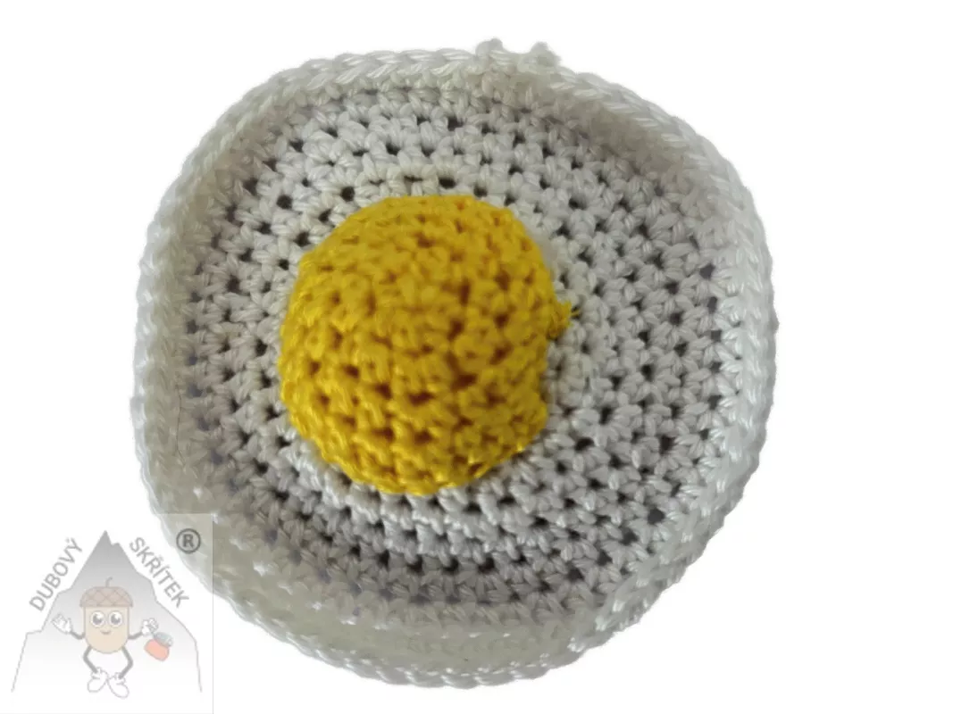 Háčkované volské oko s plastickým žloutkem uprostřed, vytvořené jako veselá dekorace.